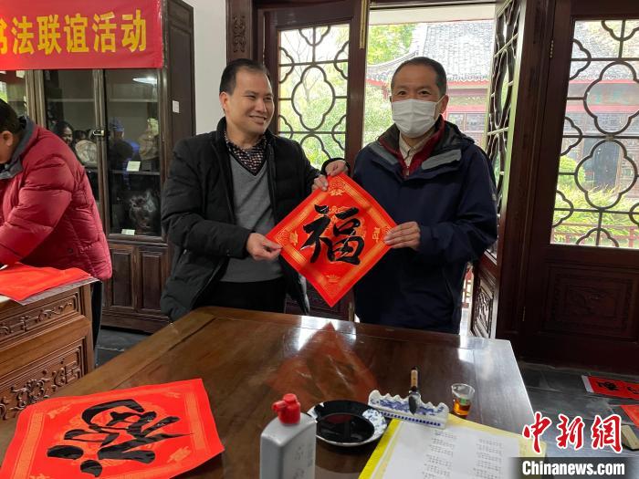 圖為一名日本人(右)展示其書寫的春聯(lián)?！×周?攝
